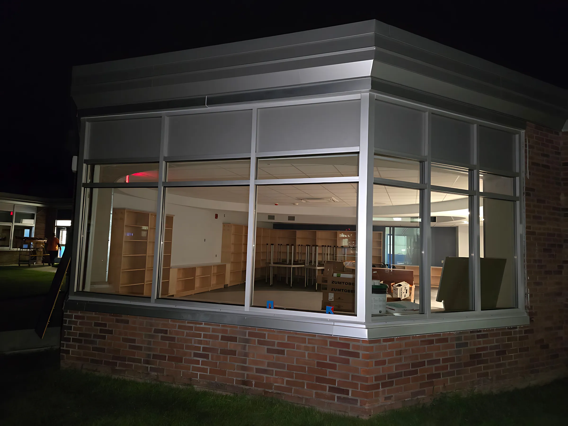 A new aluminum-framed glass corner on a brick school building, lit from inside at night