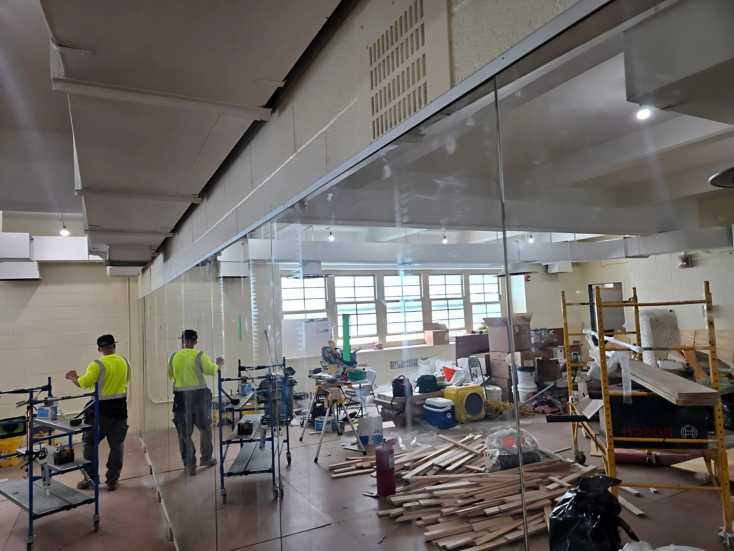 Two installers setting frameless glass partition panels in a large room