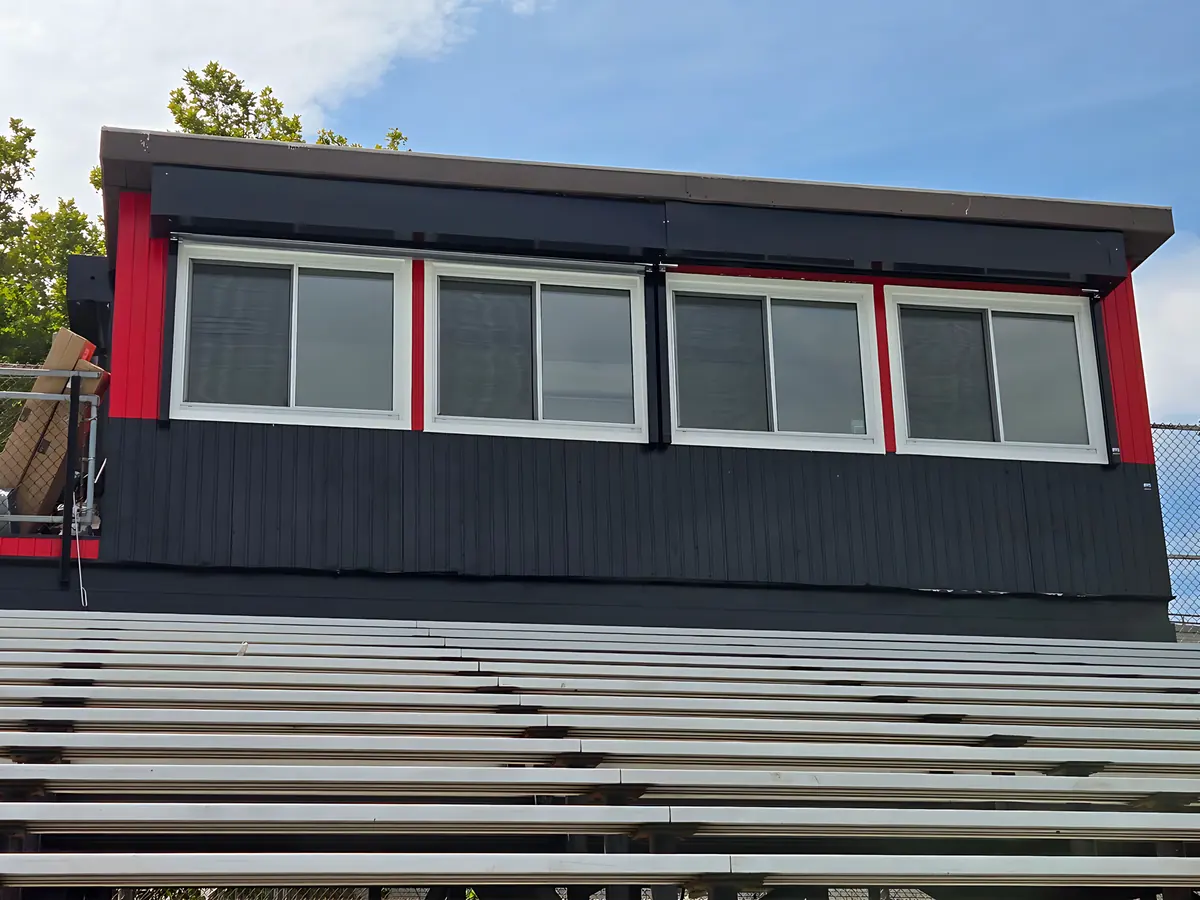 Press box above aluminum bleachers with a row of four new sliding windows