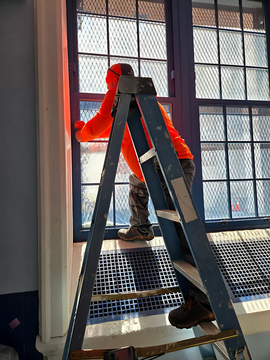 Installer on a ladder fitting a new steel-framed classroom window